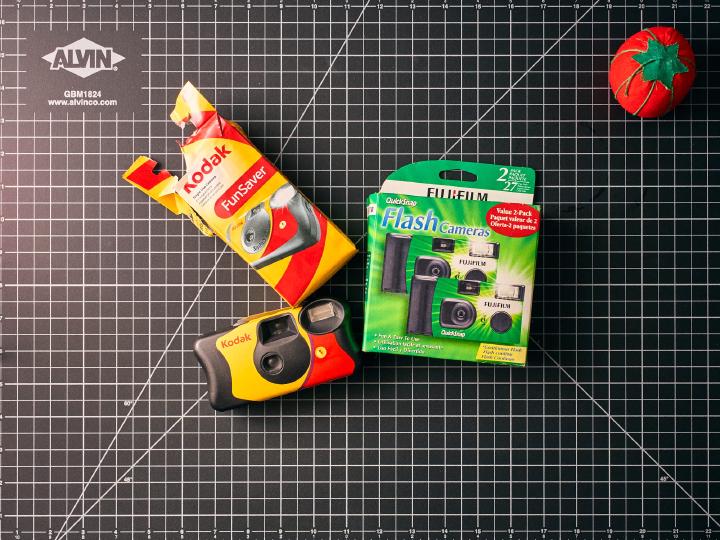 A top down view of two disposable cameras laying on a cutting mat.